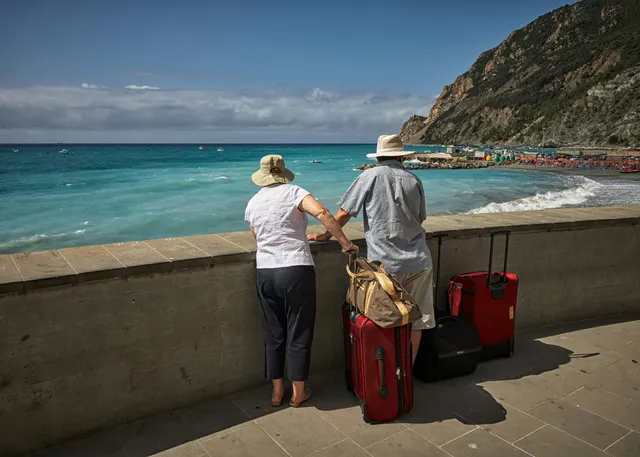 A couple pausing with their luggage to take in a coastal view while traveling abroad